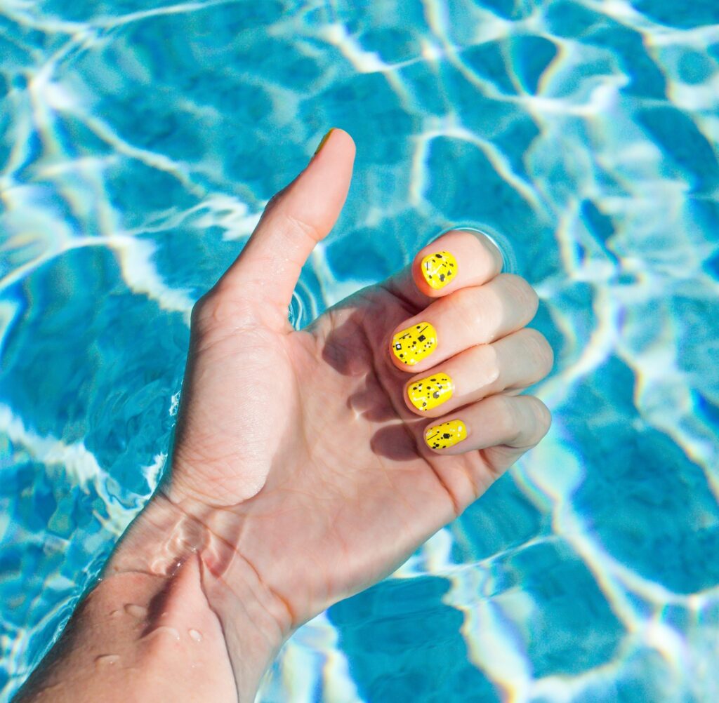 Woman's Wrist In Swimming Pool, Woman's Hand, Yellow Nail Polish Summer Fingernails